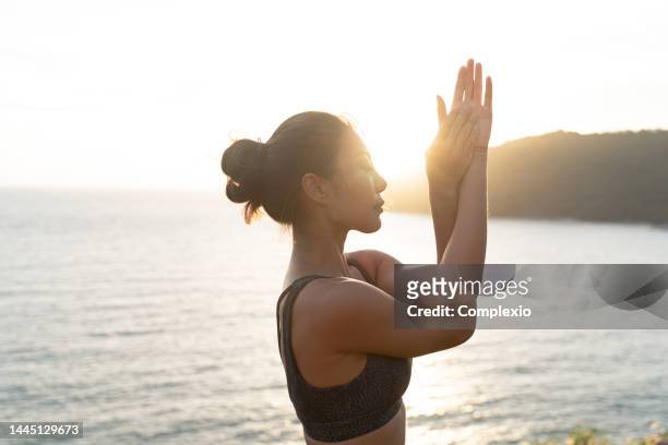 young beautiful woman doing yoga exercise on the edge of the ocean beach with copy space - sunrise yoga stock pictures, royalty-free photos & images