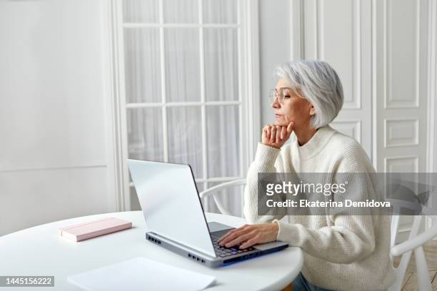senior woman browsing laptop at home - women looking at laptop stock pictures, royalty-free photos & images