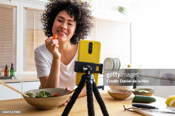 young african american female influencer tasting tomato during live stream healthy cooking tutorial. online video cooking tutorial. copy space. - cooking show stock pictures, royalty-free photos & images