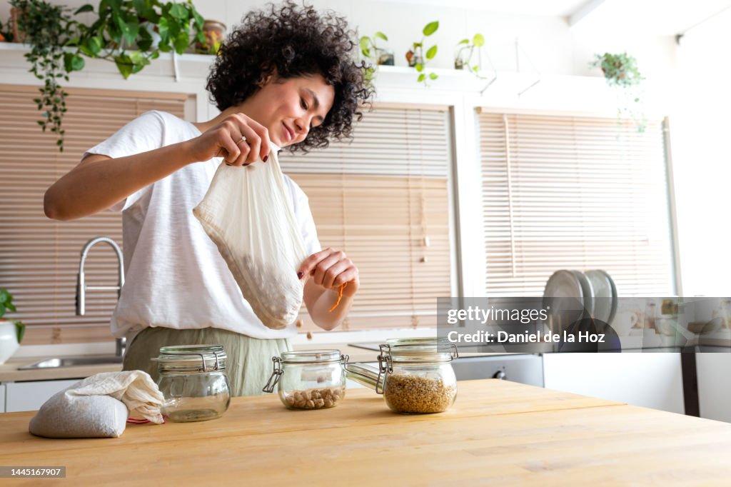 Young multiracial woman putting away chickpeas bought in bulk into glass containers. Copy space.
