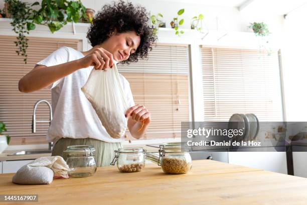 young multiracial woman putting away chickpeas bought in bulk into glass containers. copy space. - voorraadkast stockfoto's en -beelden