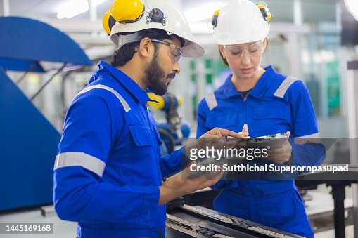 Two engineer engineer working with digital tablet for controlling the robotic arm welding production line conveyor in manufacturing.