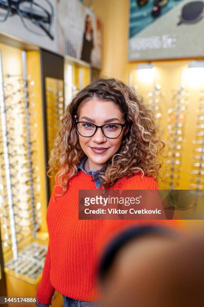 mulher jovem bonita que tira selfies enquanto experimenta óculos na loja óptica - mirror selfie - fotografias e filmes do acervo