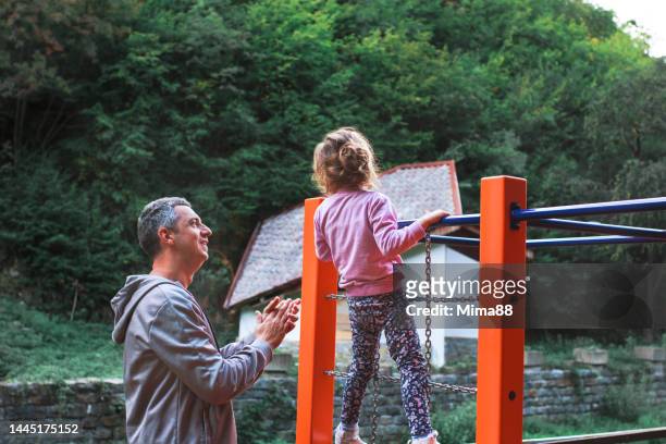 father support daughter in kids sport while she is climbing on climbing frame on playground - climbing frame stockfoto's en -beelden