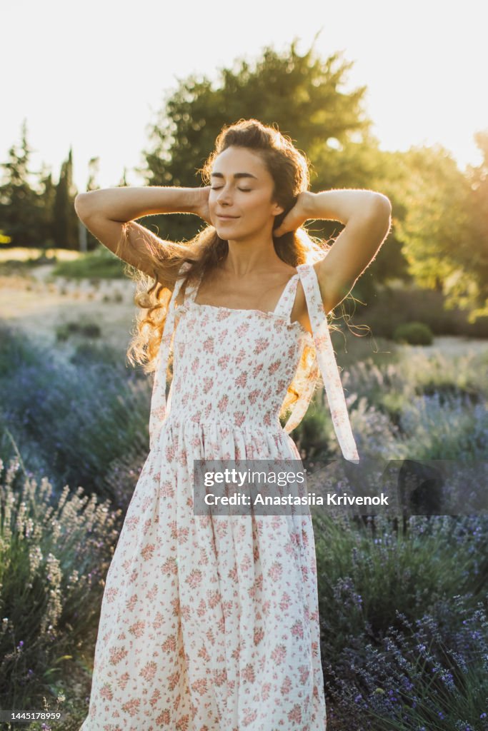 Beautiful woman with long hair in dress walking outdoor through lavender field in summer.