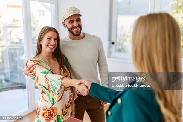 young happy couple, a pregnant woman, and an agent shaking hands in a new property - pregnant women greeting stockfoto's en -beelden