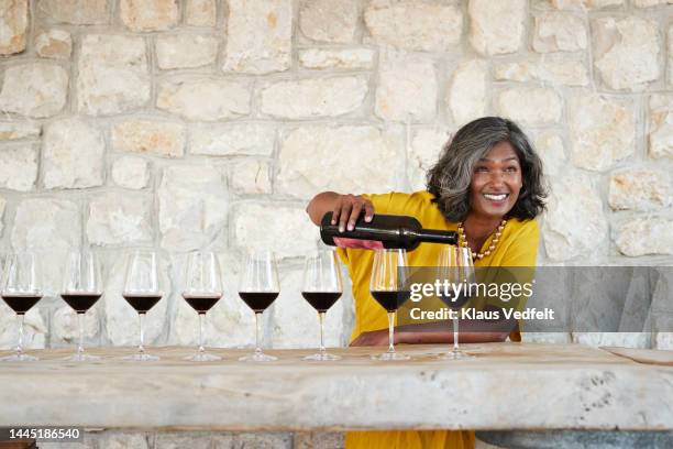 smiling female mature owner pouring red wine - same person different outfit foto e immagini stock