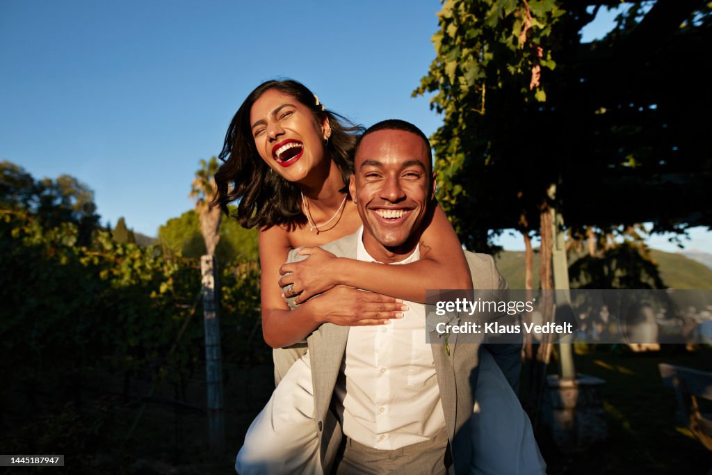 Happy groom piggybacking bride in vineyard