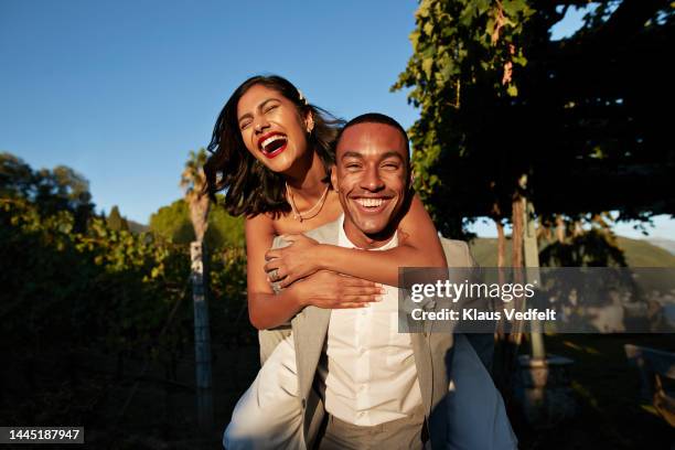 happy groom piggybacking bride in vineyard - sentiment de bonheur photos et images de collection