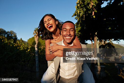 Happy groom piggybacking bride in vineyard Happy groom piggybacking bride in vineyard