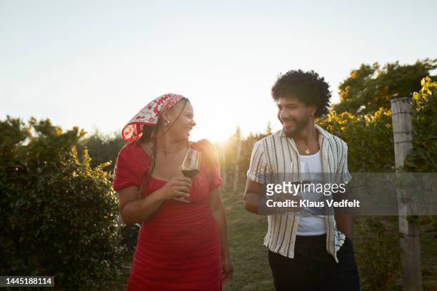 smiling couple with red wine walking amidst plants - winery stockfoto's en -beelden
