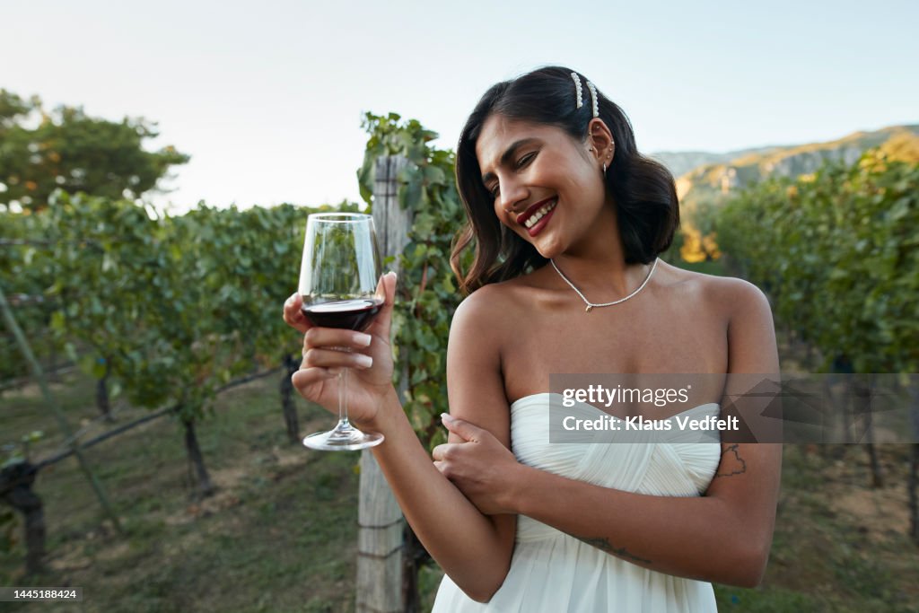 Smiling bride holding wineglass in vineyard