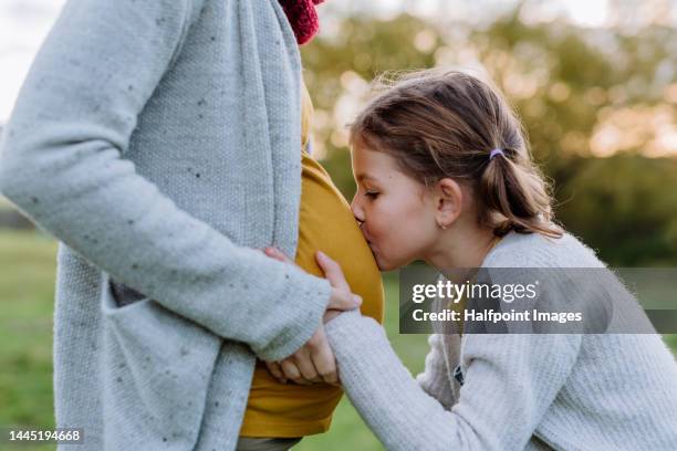 little daughter stroking and kissing pregnant belly of her mother. - kiss sisters stock pictures, royalty-free photos & images