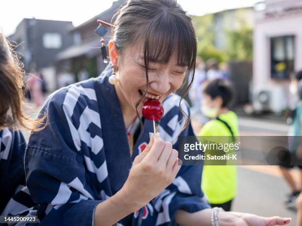 young woman in traditional japanese matsuri clothing eating apricot candy on street - happi stock pictures, royalty-free photos & images