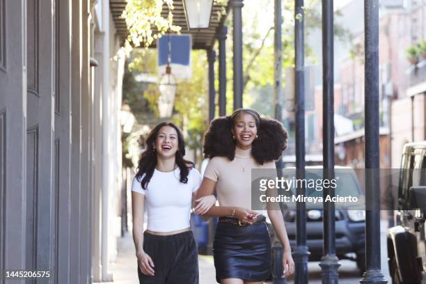 an asian generation z woman and a millenial african american woman happily walk down the sidewalk through the french quarters in new orleans during the afternoon, wearing casual clothing. - new orleans city - fotografias e filmes do acervo
