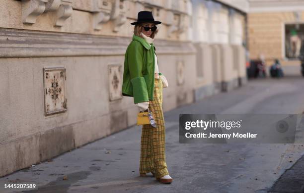 Karin Teigl is seen wearing Nomad Modern hat, Rhude black sunglasses, Hermès yellow leather mini Kelly, Baum & Pferdgarten green leather jacket,...