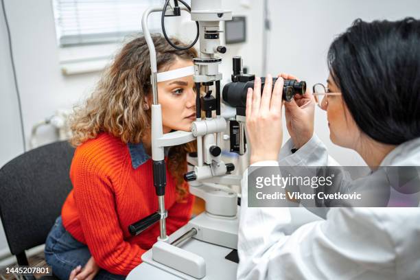 ophthalmologist performing eye exam with optical equipment on female patient - oogmeetkunde stockfoto's en -beelden