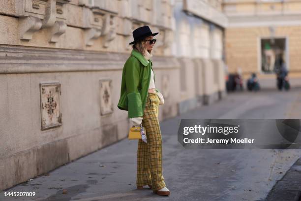 Karin Teigl is seen wearing Nomad Modern hat, Rhude black sunglasses, Hermès yellow leather mini Kelly, Baum & Pferdgarten green leather jacket,...