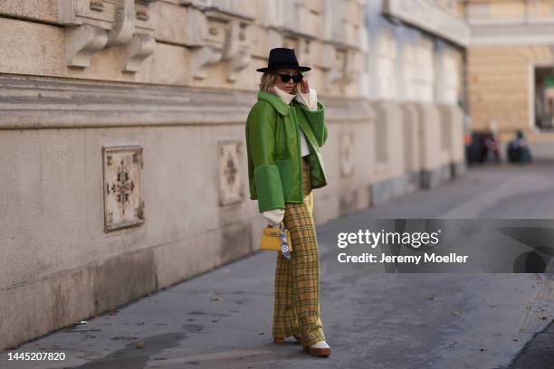 Karin Teigl is seen wearing Nomad Modern hat, Rhude black sunglasses, Hermès yellow leather mini Kelly, Baum & Pferdgarten green leather jacket,...