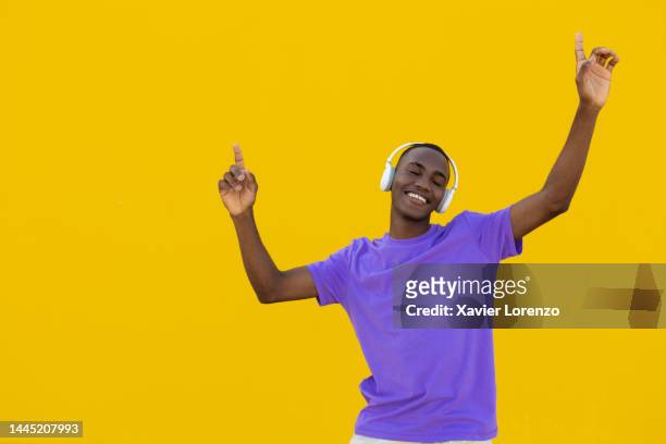 happy young black boy dancing against yellow background. - young boy enjoying music stock-fotos und bilder