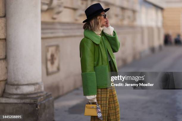 Karin Teigl is seen wearing Nomad Modern hat, Rhude black sunglasses, Hermès yellow leather mini Kelly, Baum & Pferdgarten green leather jacket,...