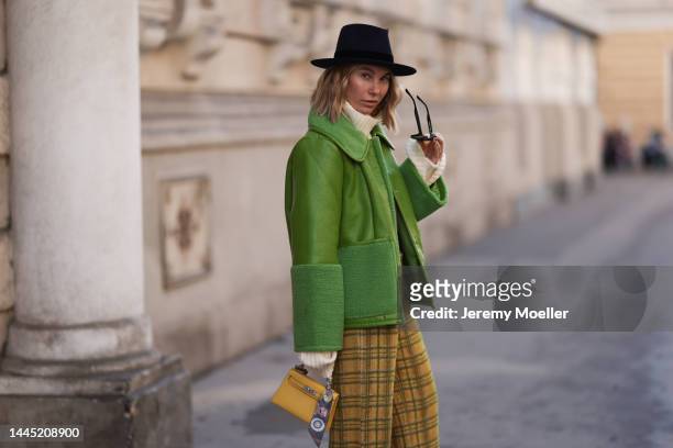 Karin Teigl is seen wearing Nomad Modern hat, Rhude black sunglasses, Hermès yellow leather mini Kelly, Baum & Pferdgarten green leather jacket,...