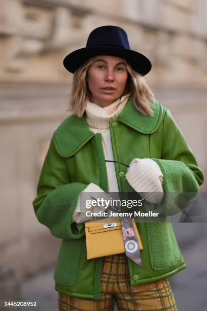 Karin Teigl is seen wearing Nomad Modern hat, Rhude black sunglasses, Hermès yellow leather mini Kelly, Baum & Pferdgarten green leather jacket,...