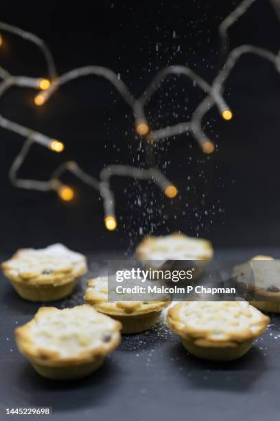 mince pies with christmas lights and icing (powdered) sugar snow - christmas mince pies stock-fotos und bilder