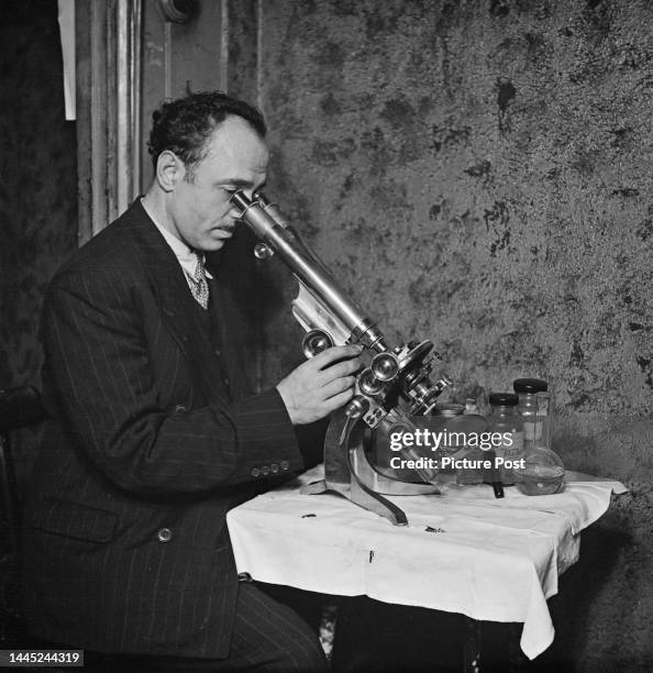 Scottish hairdresser Jack Farrell using a microscope to examine samples of cut hair at his salon in Elephant and Castle, London, January 1945....