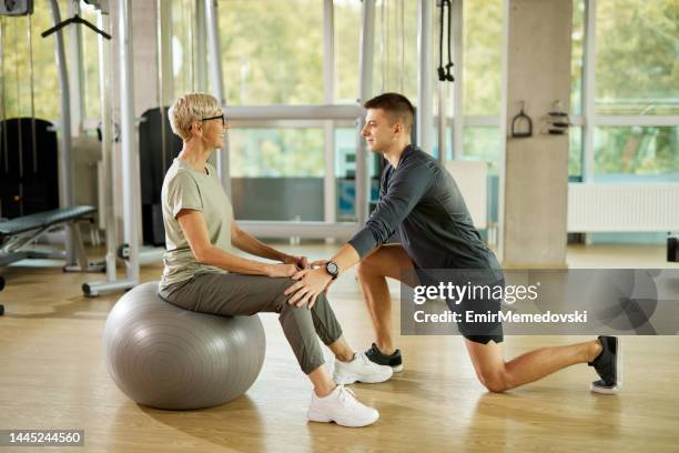 personal trainer helping senior woman exercising with fitness ball at the gym - gym excercise ball stock pictures, royalty-free photos & images