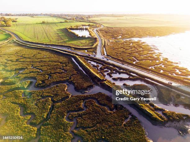 aerial view over a road running through tidal mud flats - essex england fotografías e imágenes de stock