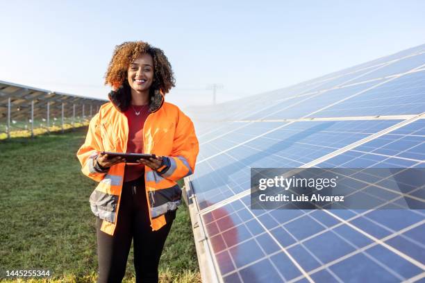 technician holding a digital tablet standing by solar grid at solar farm - industrial portraits character photos et images de collection