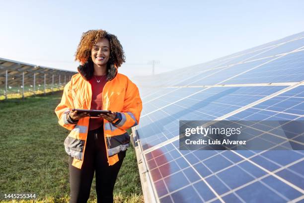 technician holding a digital tablet standing by solar grid at solar farm - electrician working stock pictures, royalty-free photos & images