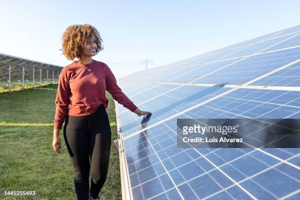 smiling woman standing by photovoltaic solar module on solar farm - same person different looks - fotografias e filmes do acervo