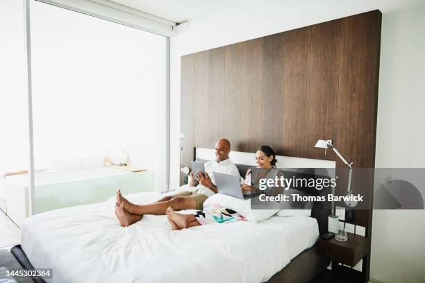 wide shot of couple working on laptop and tablet in bed in hotel room - man in suite holding tablet stockfoto's en -beelden