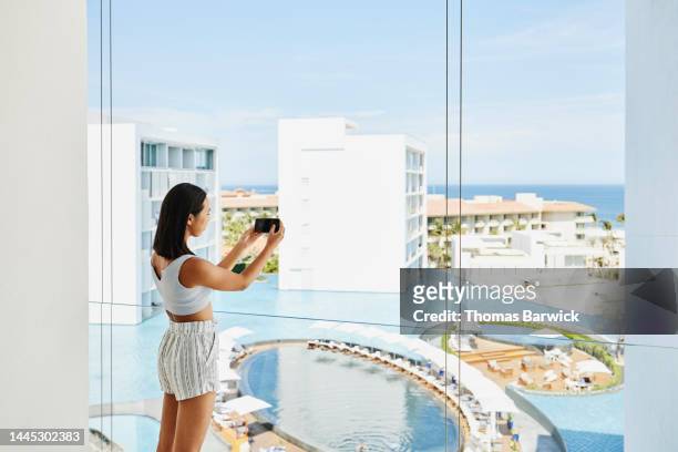 wide shot of teenage girl taking photo from deck of suite at resort - asian man suite stock-fotos und bilder