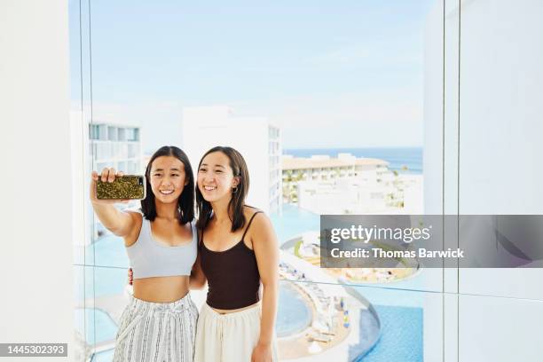 medium shot of sisters taking selfie on deck of suite at resort - asian man suite stock-fotos und bilder