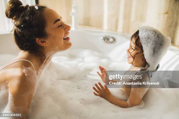 young mother and little daughter having fun in bath with foam at home. - kid bath mother stock pictures, royalty-free photos & images