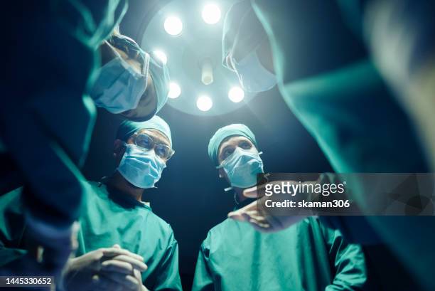 low angle four surgeons coordinating their operating cases while in the operating room, teamwork and cooperation - surgery photos et images de collection