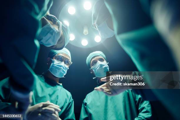 low angle four surgeons coordinating their operating cases while in the operating room, teamwork and cooperation - anesthesia mask foto e immagini stock