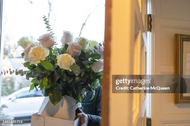 unrecognizable man standing at open front door holding fresh bouquet of roses - funeral flowers stockfoto's en -beelden