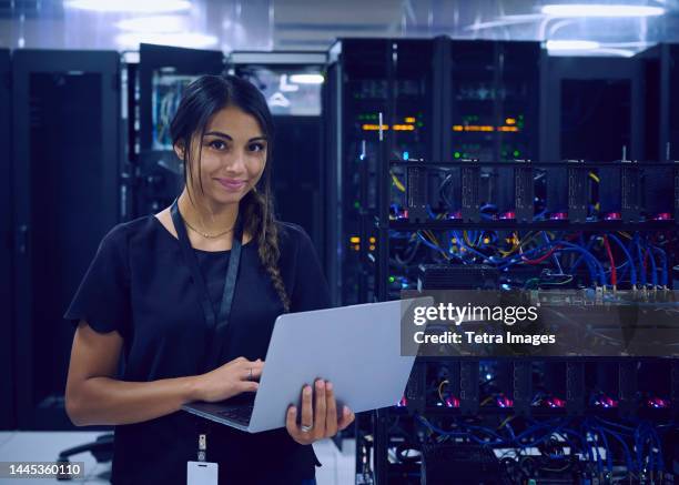 portrait of smiling female technician using laptop in server room - server room women foto e immagini stock