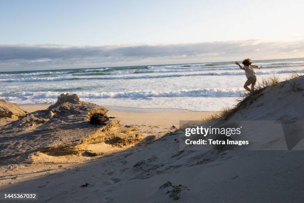 south africa, hermanus, boy (8-9) jumping on sand dune - hermanus stock-fotos und bilder