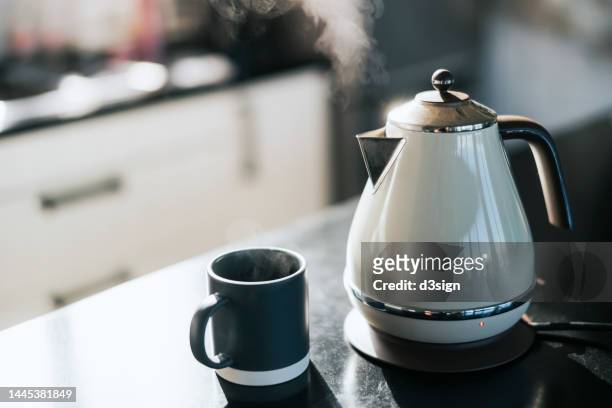 steam coming out from a kettle over the kitchen counter, with a cup by the side. time for a cup of tea in the fresh morning - bouilloire photos et images de collection
