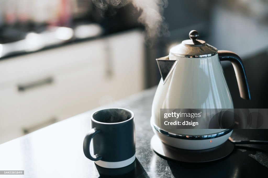 Steam coming out from a kettle over the kitchen counter, with a cup by the side. Time for a cup of tea in the fresh morning