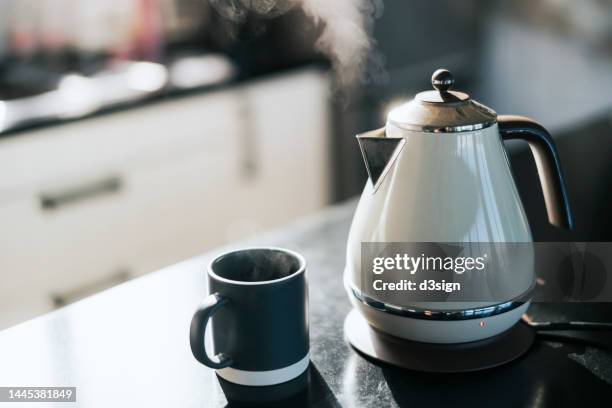 steam coming out from a kettle over the kitchen counter, with a cup by the side. time for a cup of tea in the fresh morning - boiling stockfoto's en -beelden