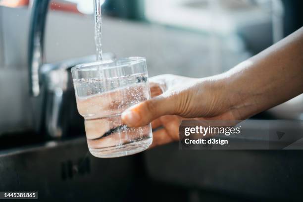close up of a woman's hand filling a glass of filtered water right from the tap in the kitchen sink at home - eau courante photos et images de collection