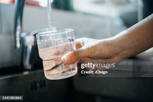 Close up of a woman's hand filling a glass of filtered water right from the tap in the kitchen sink at home Close up of a woman's hand filling a glass of filtered water right from the tap in the kitchen sink at home