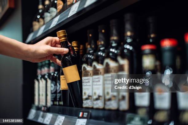 cropped shot of young woman grocery shopping in supermarket, picking up a bottle of vinegar from the product aisle. routine shopping. making a healthier food choice. healthy eating lifestyle - aceto foto e immagini stock