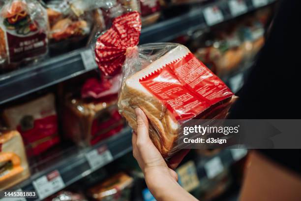 cropped shot of young asian woman grocery shopping in supermarket, shopping for fresh bakery and reading the nutrition label at the back of a packaged bread. routine shopping. healthy eating lifestyle - supermarket bread stock pictures, royalty-free photos & images